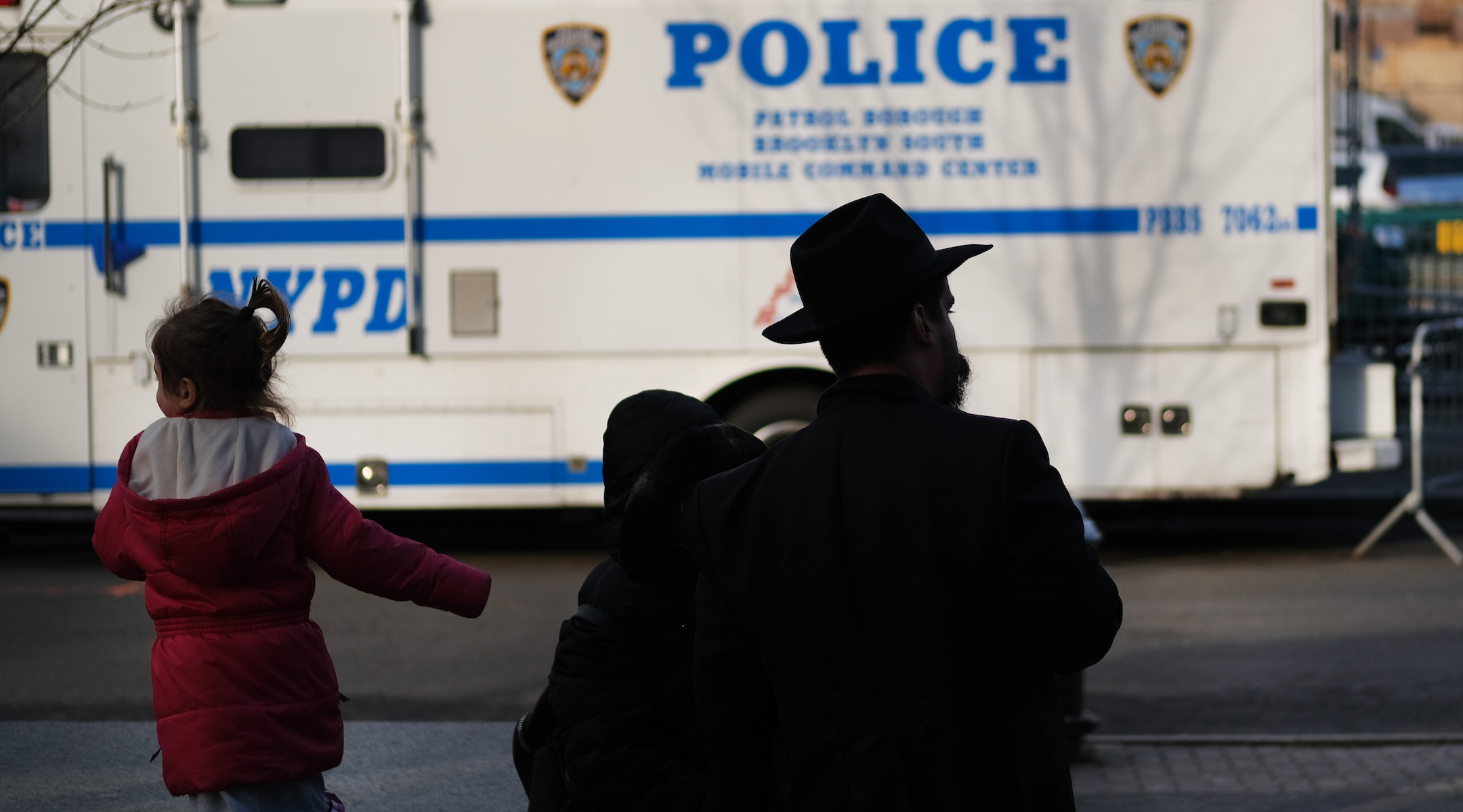 A man and girl in the Crown Heights neighborhood of Brooklyn stand opposite a police van, Dec. 31, 2019. Brooklyn was the location of more than one-third of the total number of anti-Semitic assaults committed last year, according to the Anti-Defamation League.